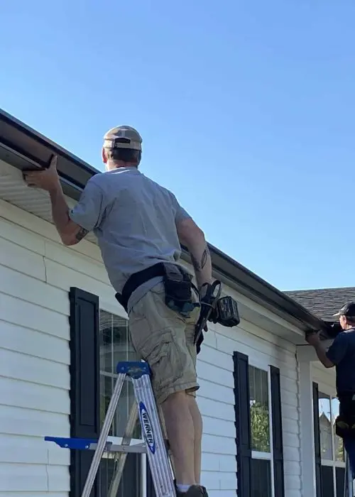 Two contractors installing new gutters on single story house