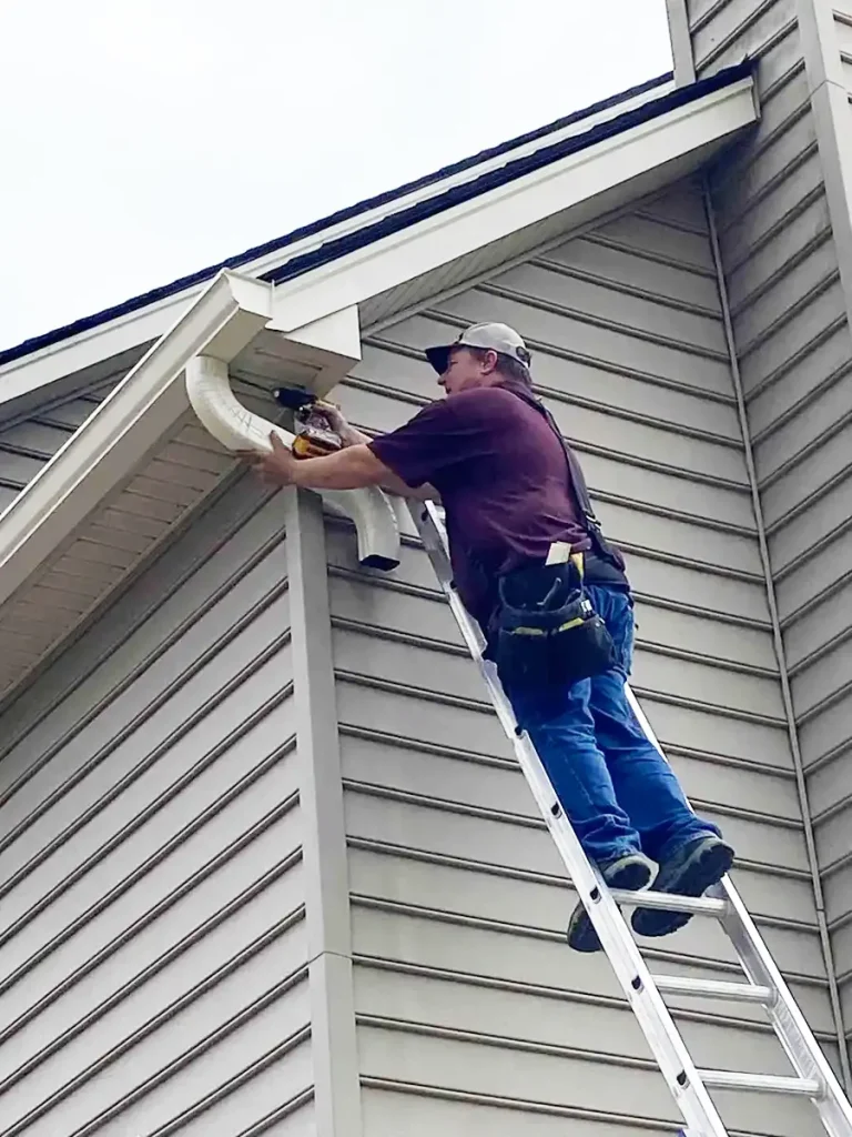 Contractor on ladder installing downspouts on residential home